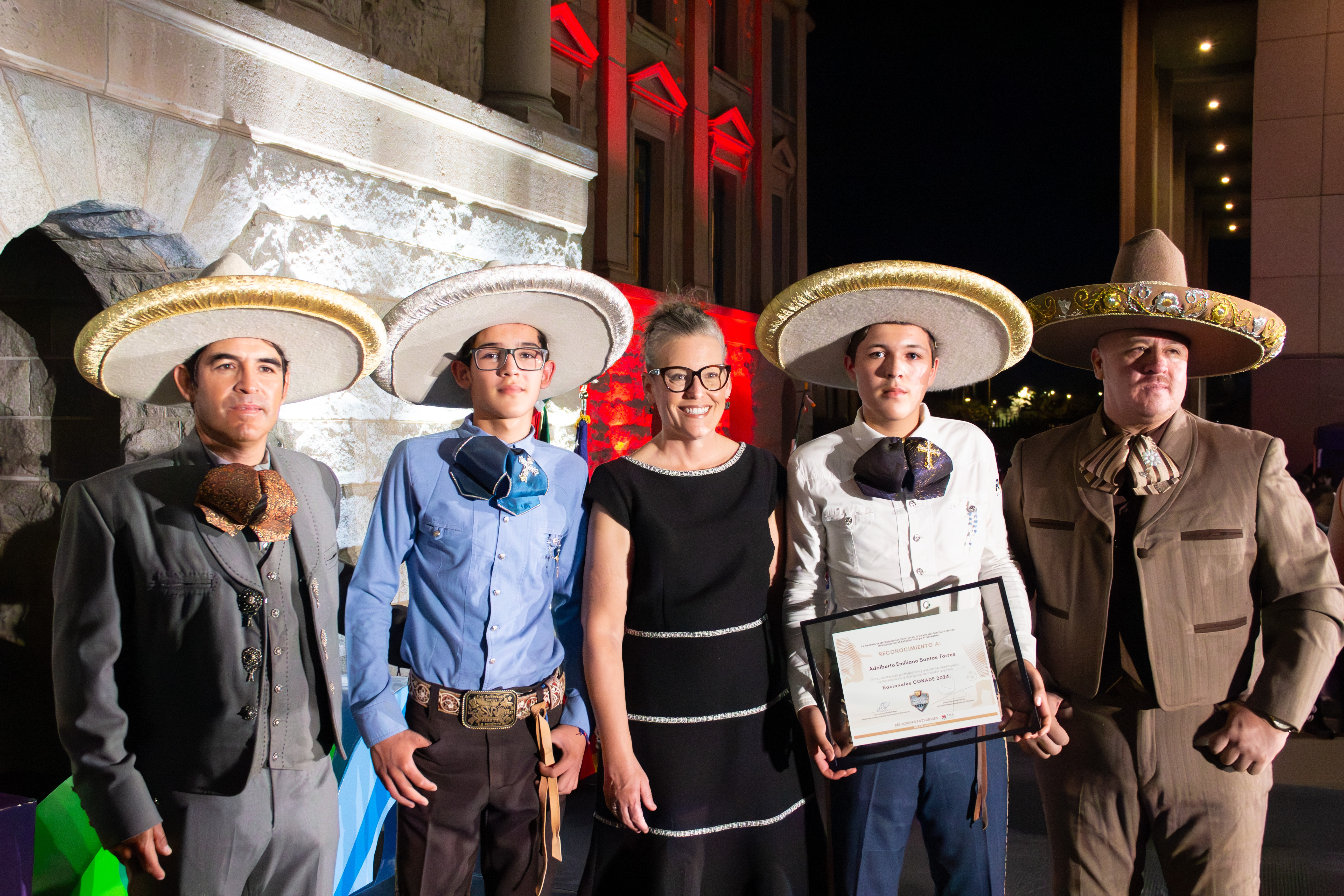 Governor Katie Hobbs surrounded by four males of varying ages in traditional Mexican clothing with one of them holding an official document.