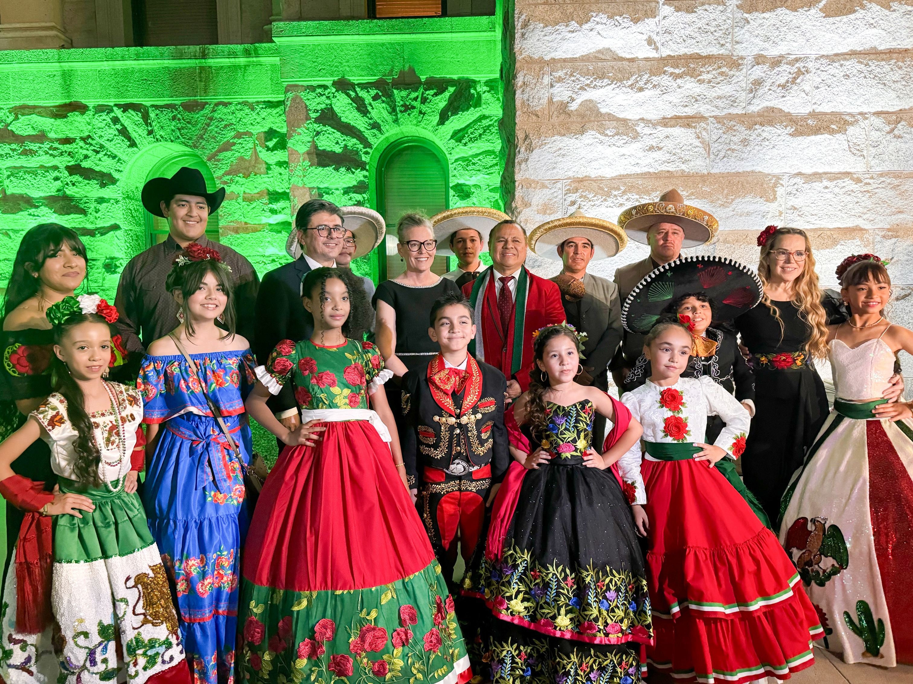 Governor Katie Hobbs surrounded by people of varying ages in traditional Mexican clothing.